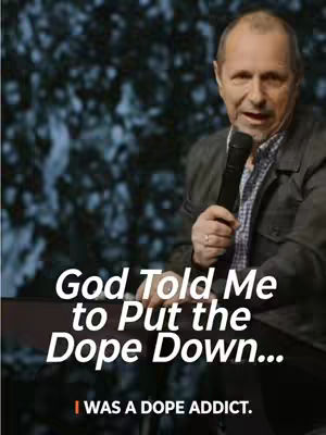 A man with short hair is speaking into a microphone. Text overlays read, 'God Told Me to Put the Dope Down...' and 'I WAS A DOPE ADDICT.' The background appears to be a blurred indoor setting with faint lights.