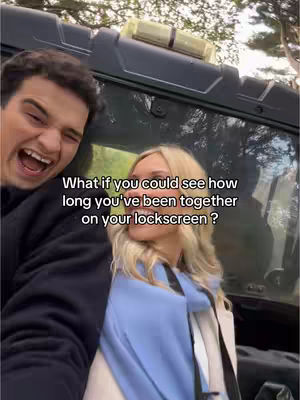 A selfie-style image featuring a couple, a man on the left with his mouth wide open in laughter, and a woman on the right, smiling and looking towards the side. The background includes the side of a vehicle. Text overlayed on the image poses a question.