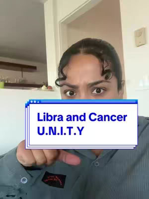 A woman with dark hair and brown eyes is in the foreground. She is covering her face with a sign that says "Libra and Cancer U.N.I.T.Y". The background is blurred and shows a door and part of a kitchen.