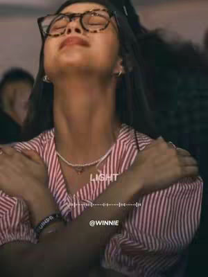 The cover photo shows a young woman with medium-length dark hair, wearing glasses, a striped red and white shirt, and a pearl necklace. Her eyes are closed, and she appears to be in a moment of worship or reflection, with her arms crossed over her chest. The background is somewhat blurred, suggesting a concert or crowded setting. Text overlays the image, including the word 'LIGHT' in white font and a sound wave graphic. The username @WINNIE is also displayed.
