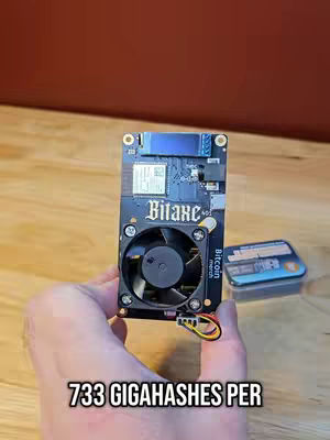 The image shows a hand holding a Bitcoin miner device, with another miner and a case in the background. The title text is overlaid at the bottom, and there is a wooden background.