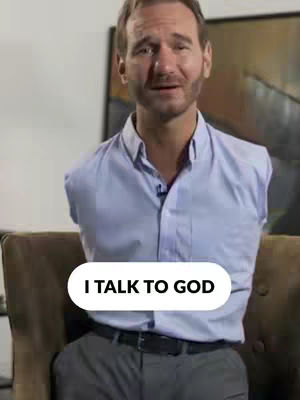 A man with a beard in a blue button-down shirt is sitting in a chair. The background has a painting and a white wall.