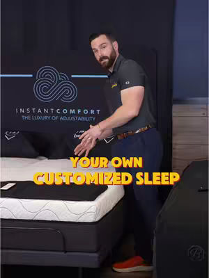 A man in a black polo shirt stands next to a mattress, gesturing with his hands towards the bed. The image is set in a store with a dark background, a logo of the product is visible on the wall.