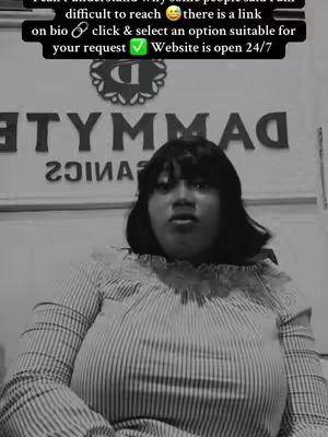 A black and white image featuring a woman centered, facing forward with a slightly open mouth; she's wearing a striped top. Behind her is a sign reading 'TYMMAG' in large letters, partially visible. Above, a text overlay provides instructions and information in a black bar, including a checkmark.