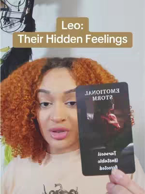 A woman with curly orange hair holds up a black card with white text, in front of a neutral background. The top of the card reads 'EMOTIONAL STORM' and details are written vertically along the side.