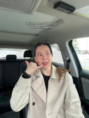 A woman sits in the driver's seat of a car, making a call-me gesture with her hand towards the camera. The interior of the car is visible, with the windshield in the background. Text is overlaid at the top of the image.