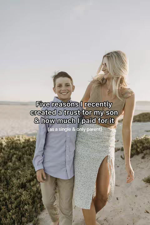 A woman and a young boy stand close together on a beach, both smiling at the camera. The woman, on the right, wears a light top and a long skirt with a high slit, while the boy, on the left, is in a button up shirt and khakis. The background shows a light sky and the ocean.