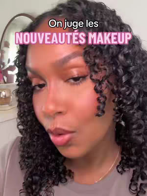 A close-up shot featuring a woman with curly hair, wearing makeup. Text overlays identify the content as a makeup review.