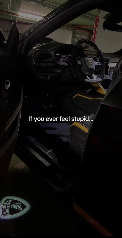 An interior shot of a black luxury car, likely a Lamborghini, with the driver's side door open. The focus is on the interior, with black leather seats with yellow accents, the steering wheel, and dashboard visible. The car is parked in a brightly lit garage. Text is overlaid on the image.