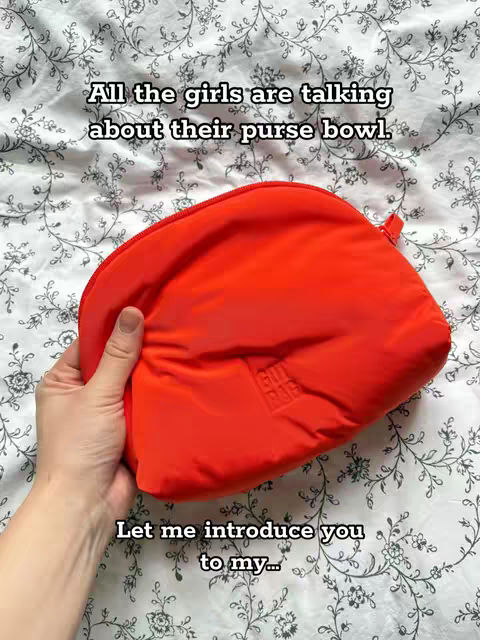 The image shows a red, puffy bag held in a hand against a background of white fabric with a floral pattern. Text overlays appear at the top and bottom.