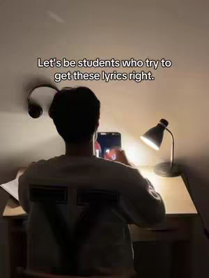 A dimly lit image showing a person from the back, seated at a desk and looking down at a tablet. A desk lamp is lit, casting light, with a pair of headphones hanging to the left.