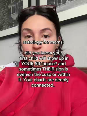 A selfie-style shot featuring a woman with dark hair wearing glasses on top of her head and a red hoodie. The background has an abstract painting and a wall. Text overlayed on the image provides information about astrology, focusing on how to connect with the personality of a child.