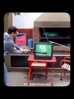 A man is shown outdoors, holding a baseball bat and about to swing at an old television set that is sitting on a small red table. Behind him, there's a brick structure with a grilling area. The image has muted colors, suggesting an overcast day.