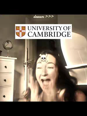 A selfie-style image showing a woman with wide eyes and an open mouth, expressing joy or surprise. Above her, a graphic reads "UNIVERSITY OF CAMBRIDGE," and a small skull decal is on her forehead. The background is a room with a partially visible door, a small side table with a mirror, and a bright light source.