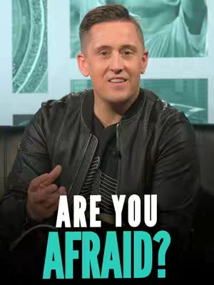 A man in a black leather jacket is seated, looking directly at the camera with a slight smile. Bold white text that says 'ARE YOU AFRAID?' is overlaid on the bottom half of the image, with the word 'AFRAID' in a bright teal color. Behind the man, a blurred background features turquoise and white geometric designs.