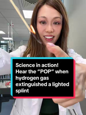 A woman in a lab coat holds a lit splint towards the camera, positioned in a lab setting. A text overlay, with a black background and white text, details the experiment. Her expression is friendly, and she appears to be explaining the experiment.