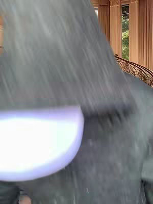 A close-up shot partially obscures a background scene with a room featuring a staircase and classical architecture.
