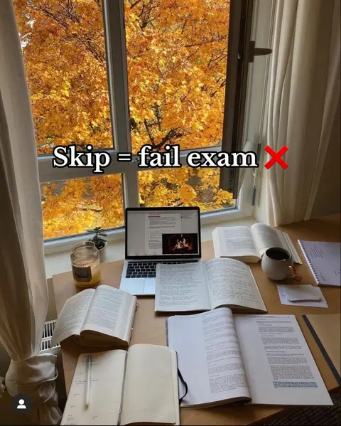 A well-lit shot of a desk set up for studying. The focus is on an open laptop displaying a document, surrounded by open books, notebooks, a mug, and a lit candle. The background features a window with a view of trees with yellow foliage, suggesting autumn. The text overlay reads, 'Skip = fail exam x'.