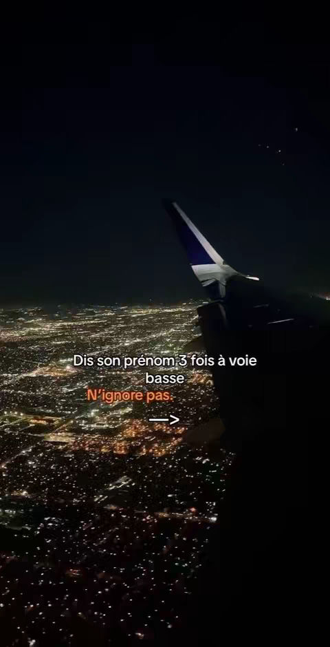 An eye-level shot taken from inside an airplane at night. The airplane wing and a fragment of the plane interior are visible in the right half of the image, with the wing featuring a dark blue and white design. Below, a city skyline sprawls across the screen, illuminated by countless lights. Overlaid on the image at the bottom left, is white text in two sections.