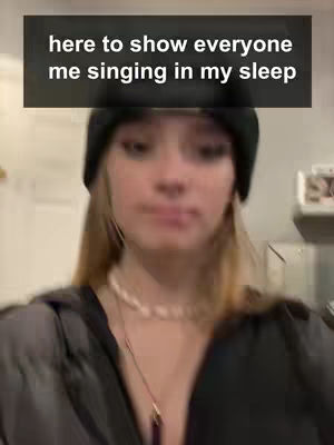 A young woman wearing a black beanie and a pearl necklace. The frame includes a dark rectangular text box with white text above her head. The woman is looking at the camera with a neutral expression. The background is blurred, with a light, indoor setting.