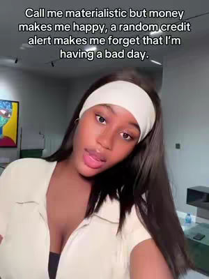 A young woman with long black hair and a white headband looks directly at the camera. She's wearing a white top. Text overlayed on the top reads, 'Call me materialistic but money makes me happy, a random credit alert makes me forget that I'm having a bad day.'