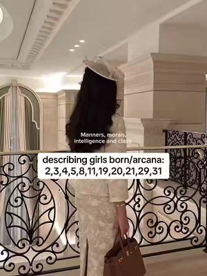 A woman stands on a balcony, the image shot from the back. She wears a light-colored outfit, a hat, and holds a brown bag. Text overlays describe “manners, morals, intelligence and class” and numerological details. The setting displays ornate railings, pillars, and detailed ceilings.
