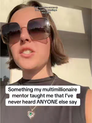 A woman with short, dark hair and sunglasses speaks directly to the camera. A text overlay emphasizes a quote from her millionaire mentor. She wears a black top and a necklace with a heart-shaped pendant.