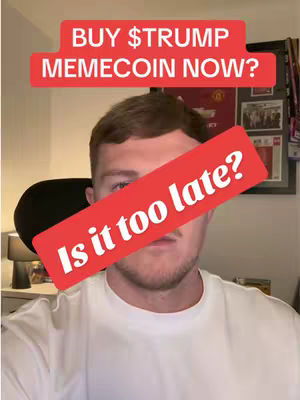 A man is centered in the frame, wearing a white t-shirt. Overlaid on his face is a red diagonal banner with white text that reads, "Is it too late?" Above his head, a red banner in a rectangular shape features the white text "BUY $TRUMP MEMECOIN NOW?" The background shows a wall with a framed image or poster, alongside some other decorative objects obscured due to the framing.