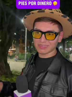 A man smiles at the camera while holding a microphone and wearing sunglasses and a straw hat. A text overlay is visible.