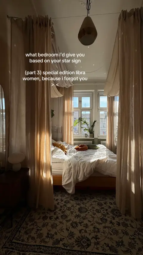 A well-lit bedroom with a four-poster bed draped with sheer curtains, creating a cozy, enclosed space. Natural light streams through a large window, illuminating the room. The bed is made with white linens and decorative pillows, and a patterned rug covers the floor.