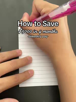 A close-up shot of hands writing on a lined notepad with a pink pen. The text overlay reads 'How to Save $5000 in 4 months -biweekly pay-'. The background is a dark surface.