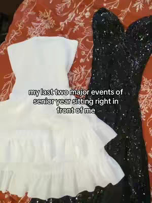 The cover image presents two dresses, one white and the other black, draped on a red floral patterned surface, likely a bedspread. The white dress is a short, sleeveless dress with tiered ruffles. The black dress is a long, sequined gown. Text overlay at the bottom left. The overall composition has an aesthetic, personal feel.