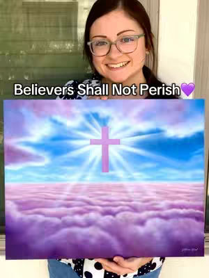 A woman with glasses is smiling, holding a painting of a cross in front of a sky with clouds. The painting features a pink cross in the center of a bright, radiating light, set against a blue sky and a layer of what appears to be pink clouds below. The background visible behind the woman includes part of a window and a wall.