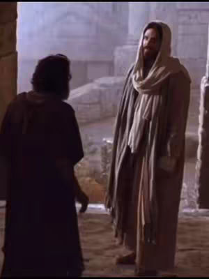 An image from a film featuring Jesus Christ and another man. Jesus is to the right, wearing a white hooded robe with a scarf. The other man is on the left, turned away from the camera.