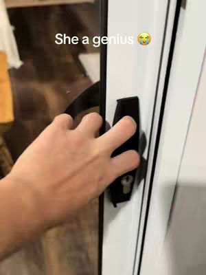 A hand is grasping a black door handle on a white door. The focus is on the hand and handle, with the background blurred.
