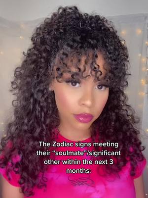 A close-up shot of a woman with curly hair and heavy makeup, wearing a pink top, with text overlaid and a background. The woman is centered, with her face clearly visible, and the background appears slightly out of focus with fairy lights visible.