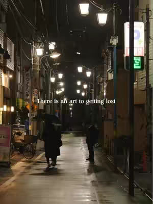 An alleyway at night in a city with lights illuminating the path. The ground is wet with reflections. Two figures are walking away from the camera. Text is overlaid on the image.