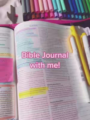 An open Bible is the central focus, with the text of the pages visible. Text overlayed on the Bible says "Bible Journal with me!" Colorful markers are arranged at the top of the image, and a pink and white marker sits on the right.