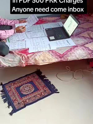 A person is working on a laptop with some papers spread out on the bed with a decorative rug on the floor.