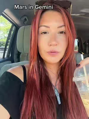 A woman with long red hair sits in a car, a drink in her hand. Text overlays the top of the frame.