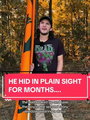 A man holding an orange flag with a flag person wrapped around it and black text over a red block at the bottom. He wears a black t-shirt, a black cap, and light-colored pants. The background is filled with autumn-colored trees.