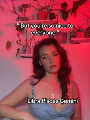 A woman with long, wavy brown hair is the central focus, dressed in a blue denim top. The background is illuminated by a red light, with plants and shelves visible behind her. Text overlays identify her astrological signs.