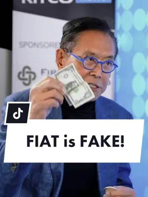 The cover image shows a man holding up two US dollar bills while looking at the camera. A white banner with the text "FIAT is FAKE!" is placed at the bottom of the image over the man. The man is wearing glasses, a blue blazer, and a black shirt.