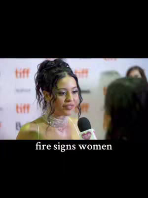 A woman is being interviewed with a microphone in the center. Below her is a text overlay that says 'fire signs women'. The background is blurred, but appears to be red, and includes the word 'tiff' repeated.