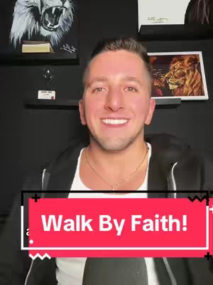 A man in front a dark backdrop, wearing a black jacket over a white shirt, smiles at the camera. The background contains framed art pieces and an art shelf. A rectangular graphic with the words "Walk By Faith!" is in the lower middle.