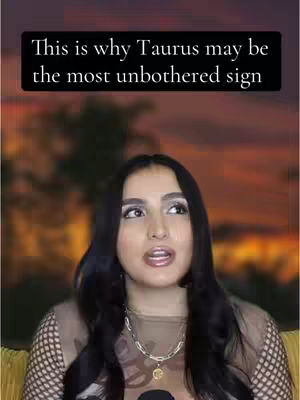 A woman with long black hair is looking up and slightly to the right, with her mouth open. A black text box at the top of the image says, "This is why Taurus may be the most unbothered sign". The background is a blurry mix of orange and yellow, suggesting a sunset or warm lighting.