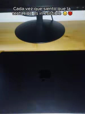 The image shows a top-down view of a desk with a monitor and a laptop. The text overlay is white and placed at the top. The background includes a wooden table with a black monitor support base.