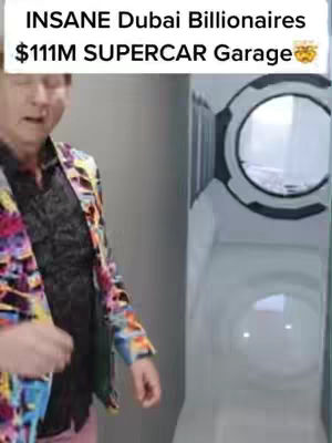 A man in a colorful jacket looks towards the camera. Text overlays at the top indicate the video's subject, and a blurred background of a futuristic garage or car storage area is visible.