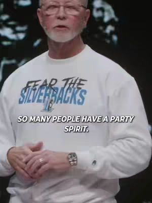 The image shows a man in a white sweater with text that says "FEAR THE SILVERBACKS". The man is wearing glasses and has a white beard. He is standing in front of a blurred dark background, with text overlayed at the bottom