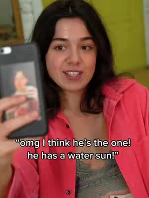 A young woman holding a phone in front of her face, displaying an image, while smiling. She's wearing a red button-down shirt over a patterned top. Text overlays at the bottom. The background is out of focus, but hints at a room or interior setting.